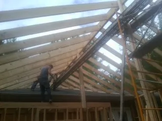 Rafters going up over a new addition with a worker on the wall in Sussex