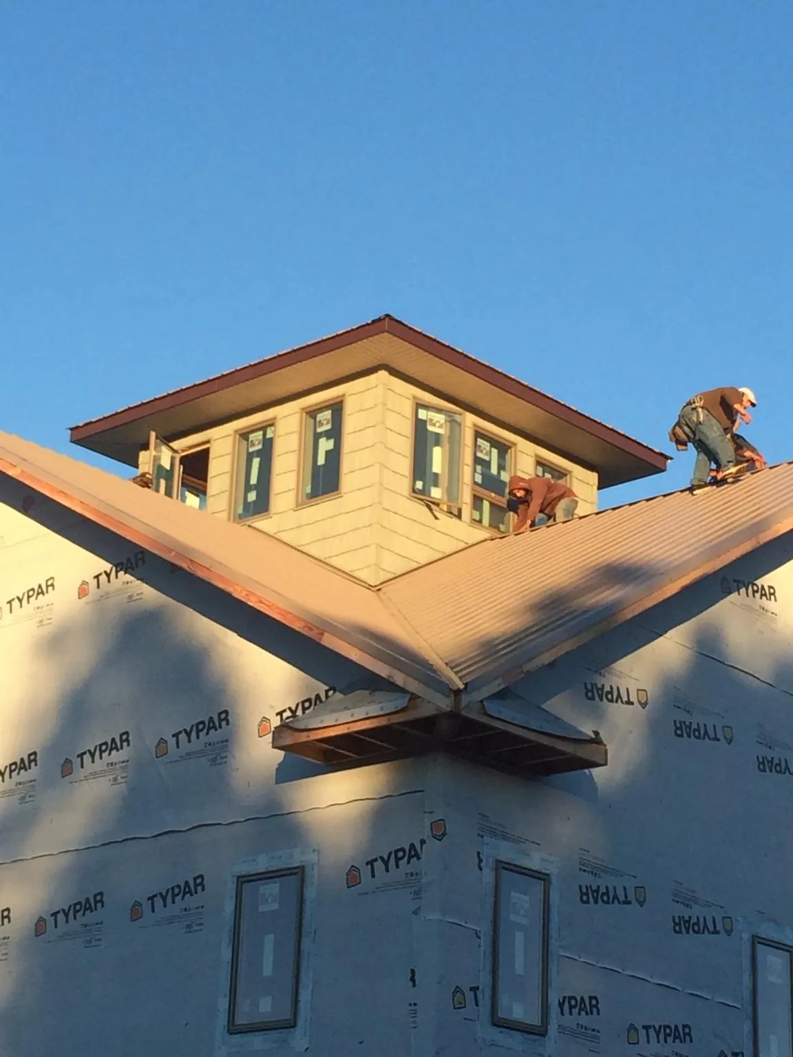 Roofers working around a rooftop cupola on a new metal roof at sunset — Roof Waterproofing in Sussex by Roofing Brothers